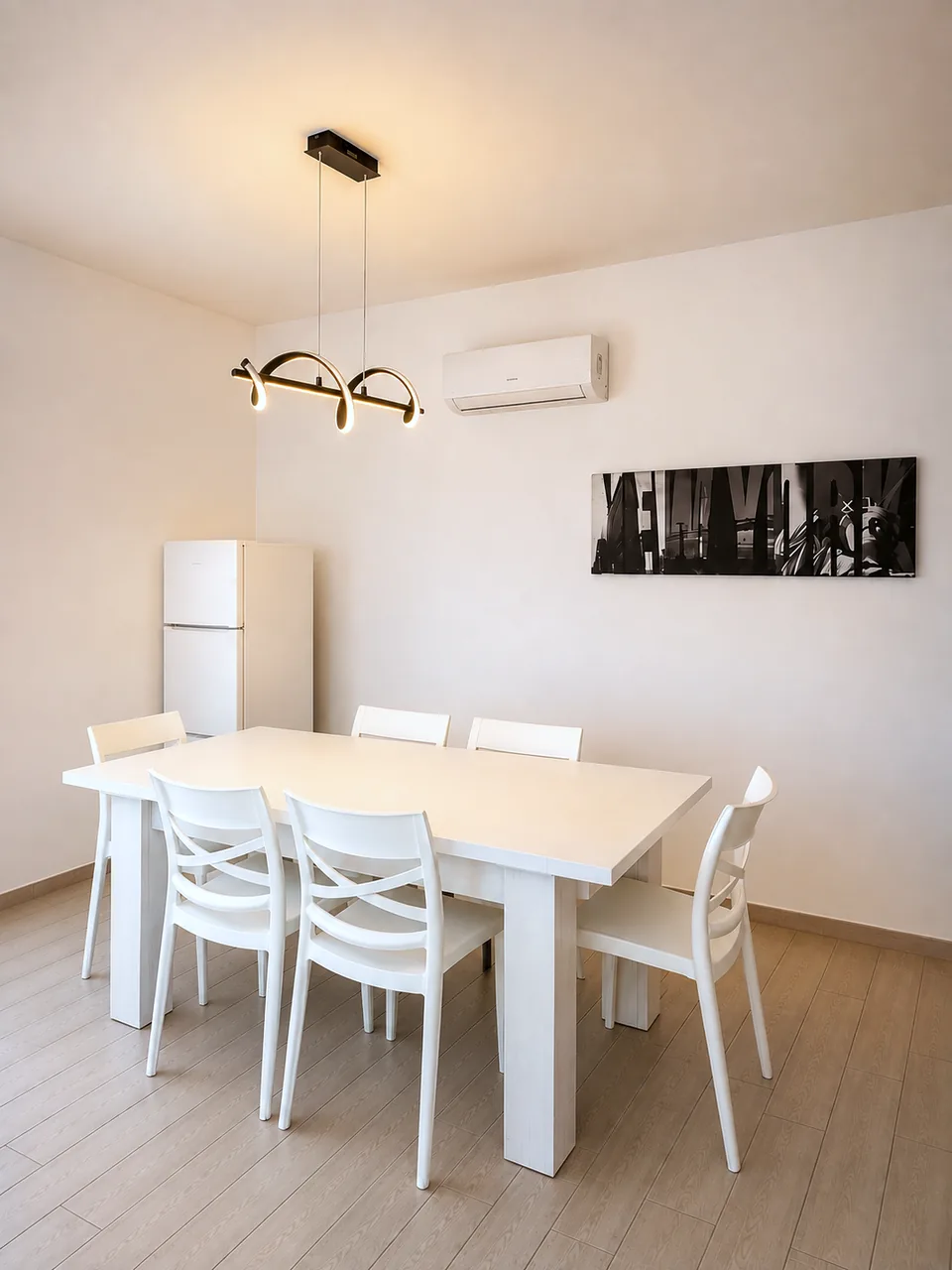 White dining table with six white chairs under a sculptural black pendant light at La Dolce Vita