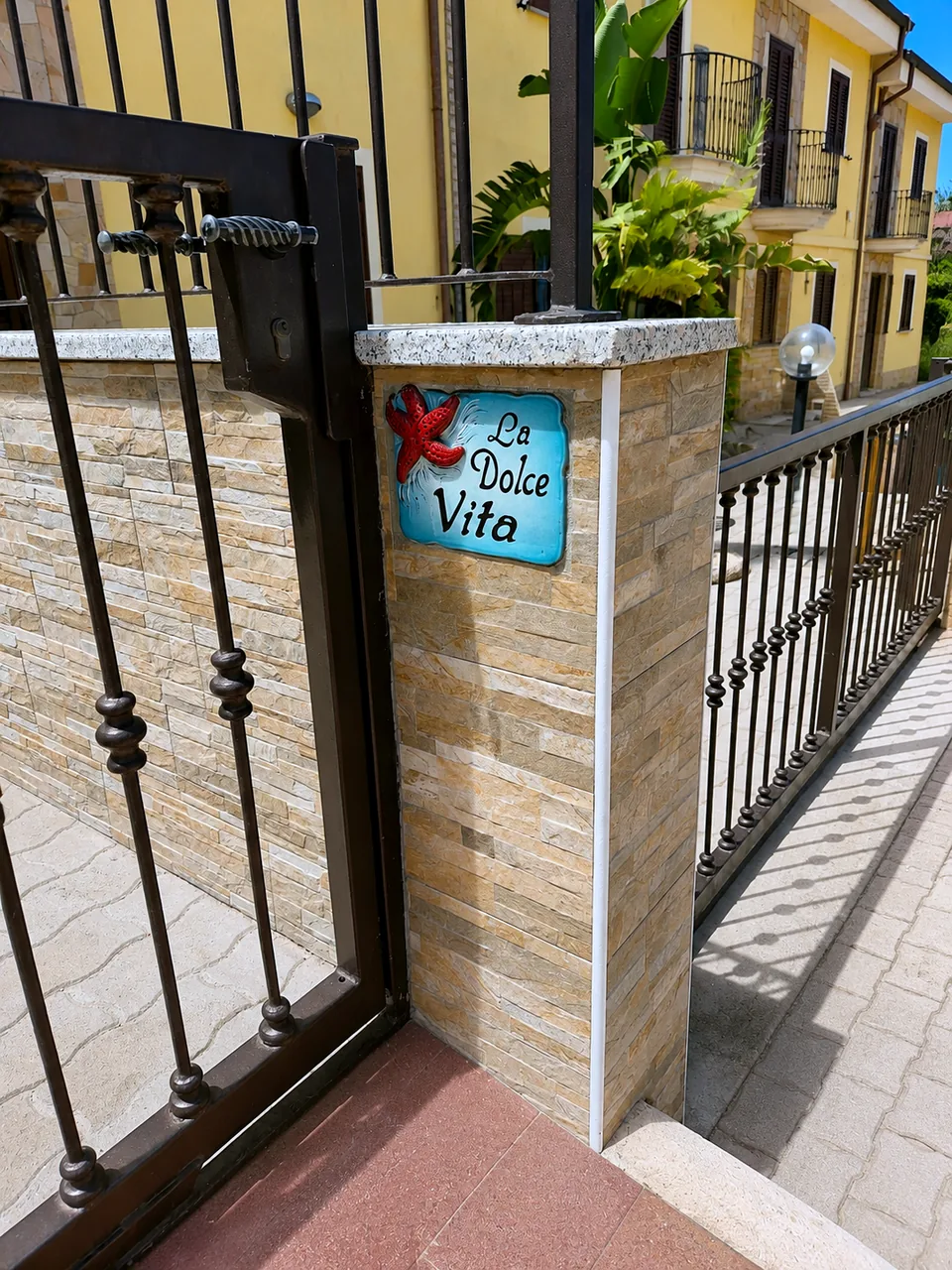 Private entrance gate to La Dolce Vita with a hand-painted ceramic starfish sign on the stone-clad pillar
