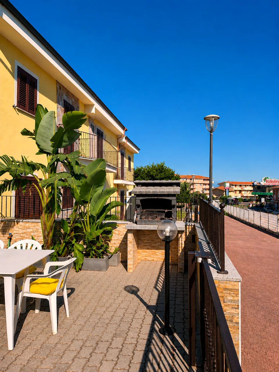 Outdoor terrace with barbecue, tropical plants and dining area looking onto the street in Valledoria