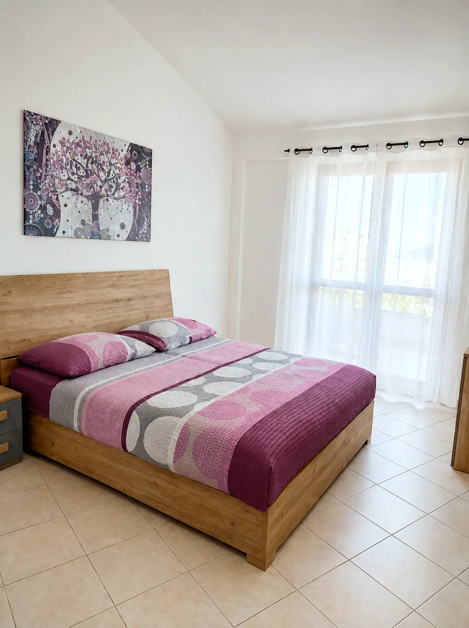 Master bedroom double bed in bright natural light beside sheer-curtained balcony doors