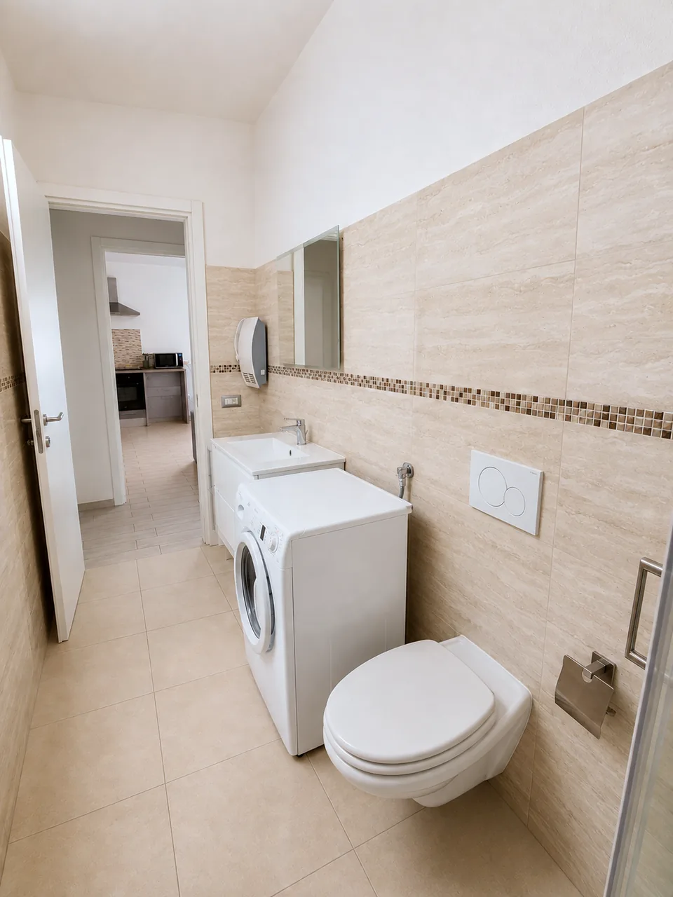 Bathroom at La Dolce Vita with white floating vanity, large mirror, washing machine and travertine-look tiles, looking through to the kitchen