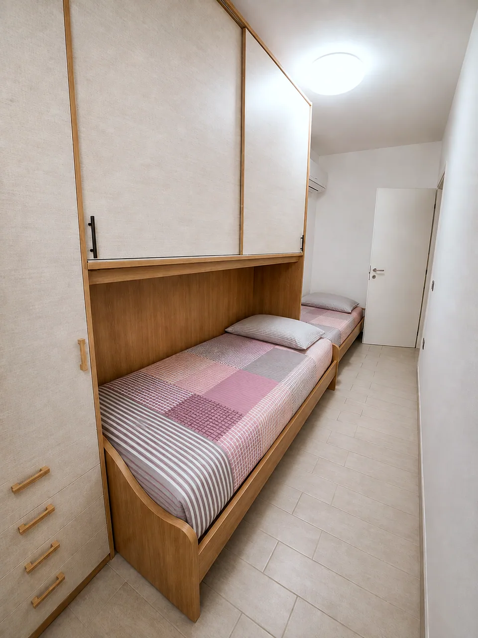 Second bedroom at La Dolce Vita with two oak single beds, pink checked bedding and floor-to-ceiling fitted wardrobes