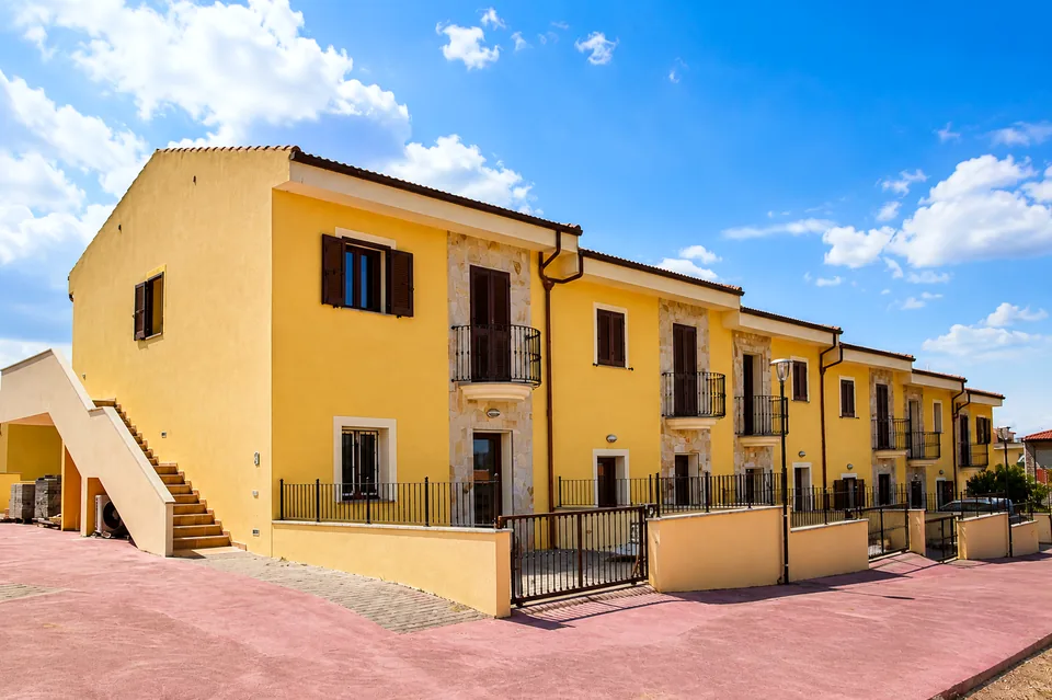 Exterior of the yellow La Dolce Vita apartment building in Valledoria, Sardinia, with wrought-iron balconies and a terracotta roof