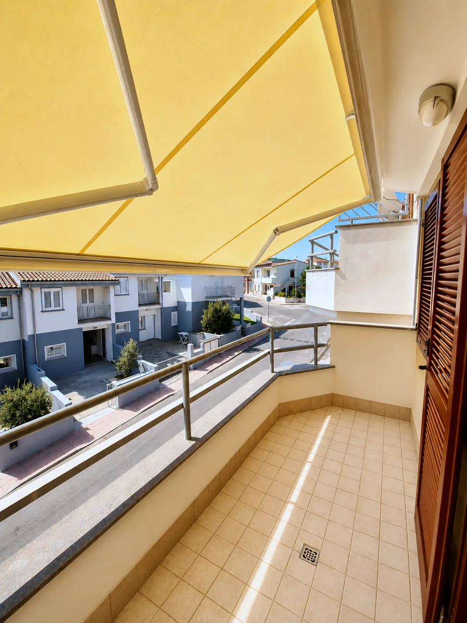 Rear balcony off the second bedroom, shaded by a yellow awning with tiled floor and village outlook