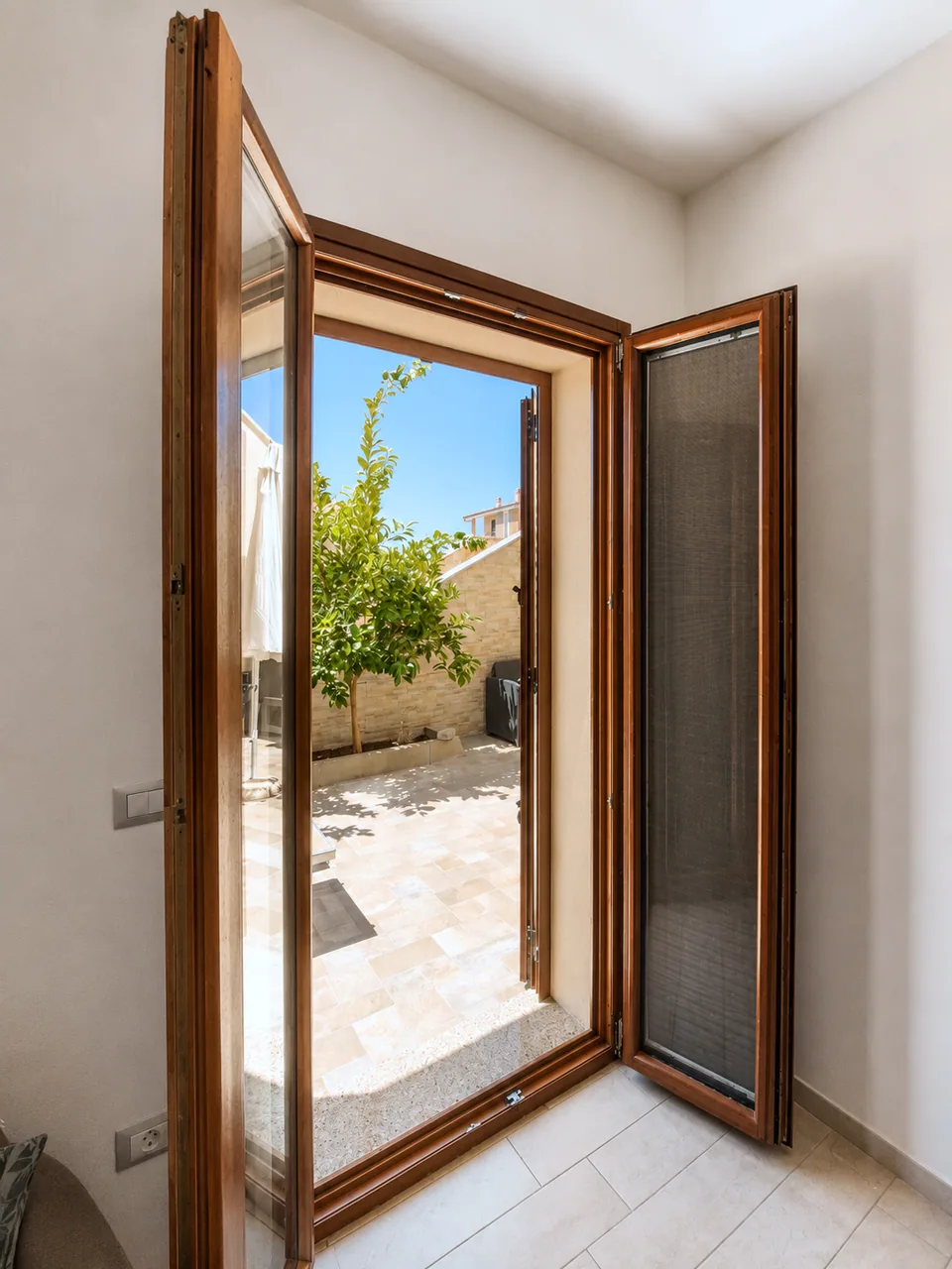 Open wooden patio door in the La Dolce Vita master bedroom leading out to the sunlit terrace with a lemon tree and parasol