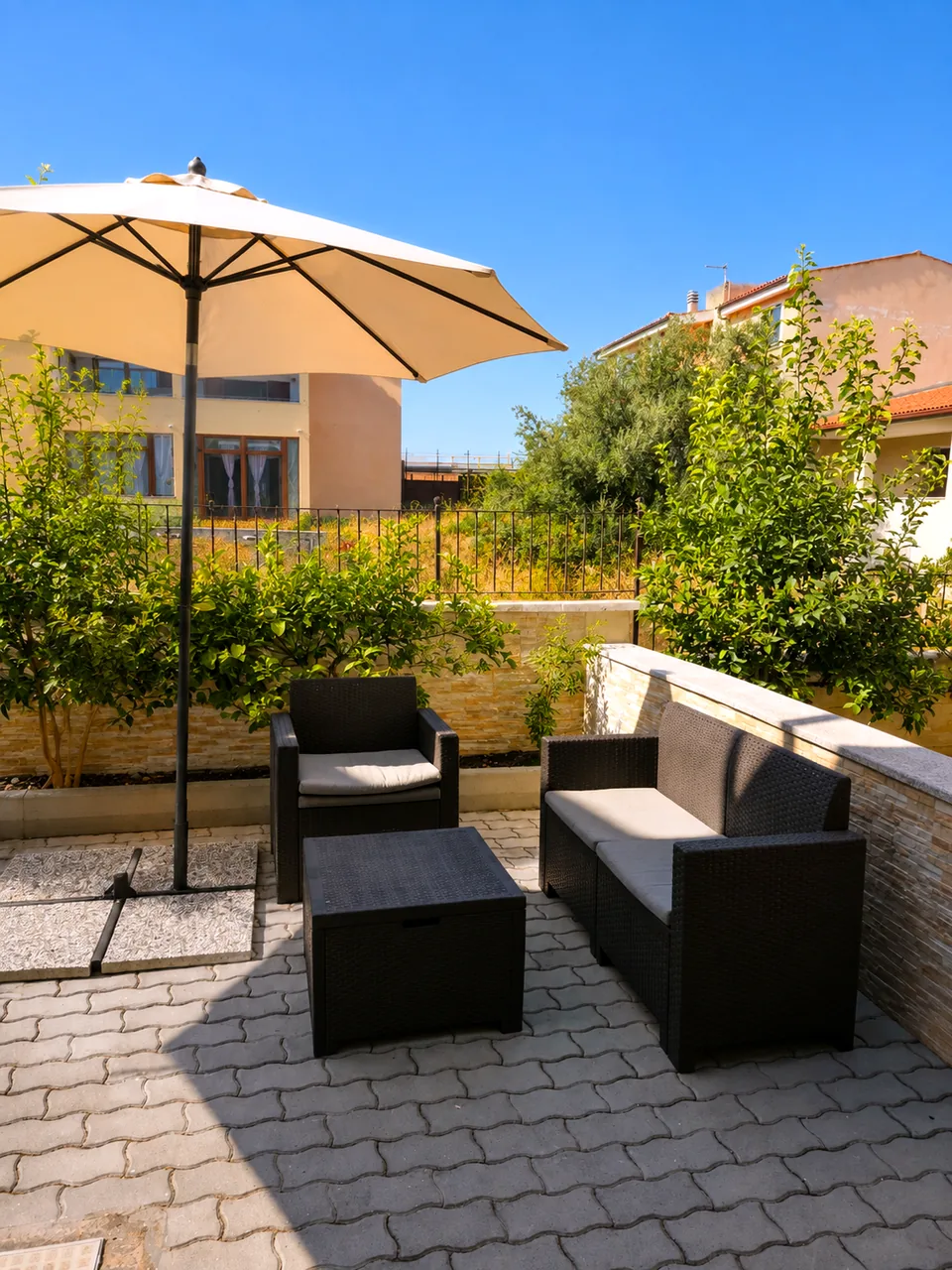Rear garden terrace at Il Paradiso leading out from the bedrooms, with a rattan sofa, armchair, coffee table and cream parasol on interlocking paving