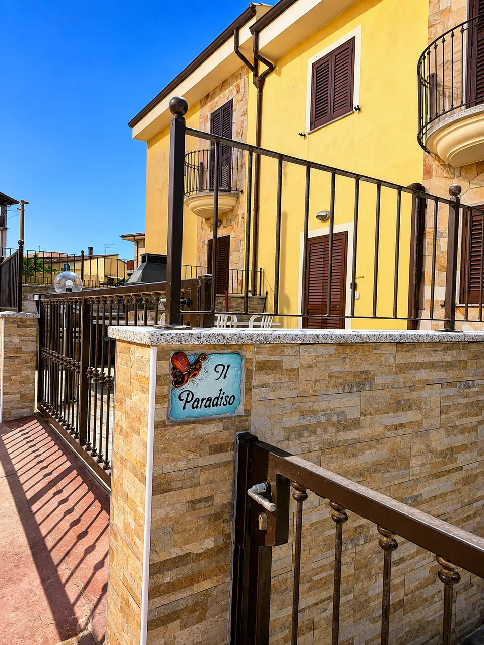 Hand-painted ceramic Il Paradiso sign with an octopus motif on the stone-clad entrance wall of the yellow apartment building in Valledoria, Sardinia