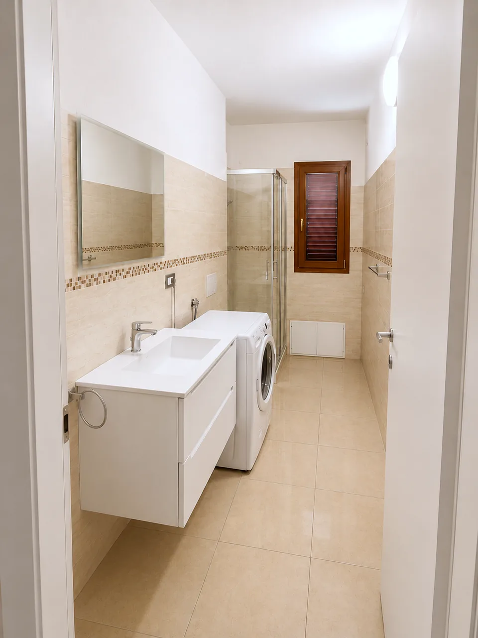 Full view of the La Dolce Vita bathroom with white vanity unit, washing machine, corner shower and heated towel rails