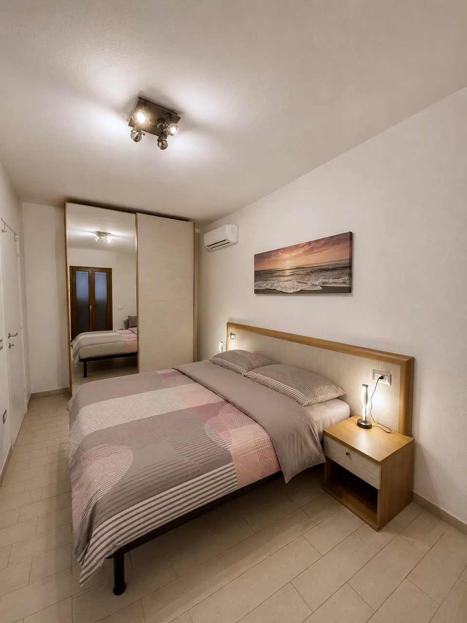 Master bedroom at La Dolce Vita with mirrored fitted wardrobe, bedside lamp lit and sea sunset artwork on the wall