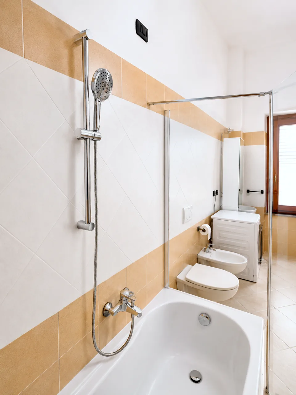 Bathtub shower head and mixer tap detail against cream and honey tiling