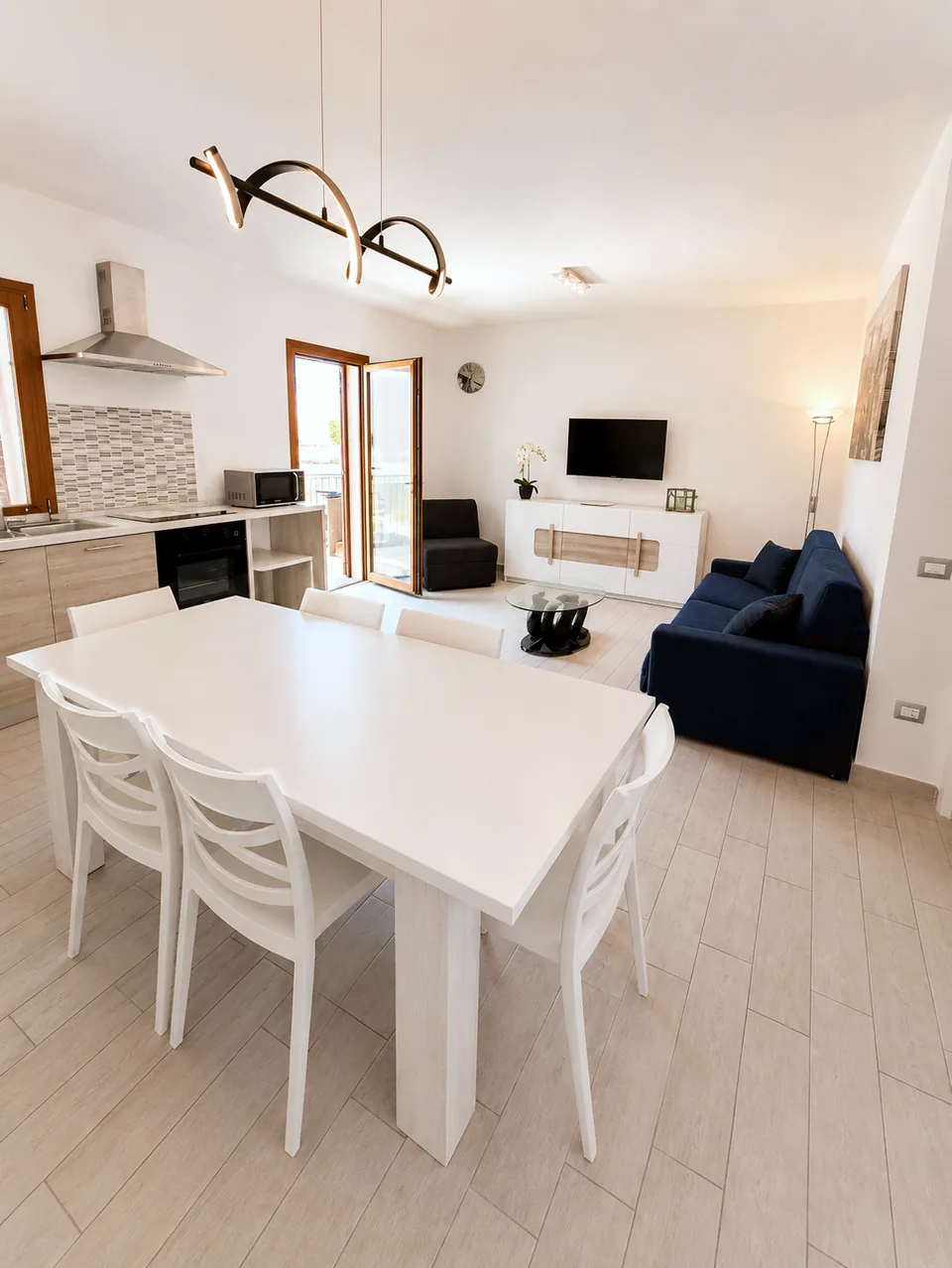 Open-plan living, dining and kitchen at La Dolce Vita in daylight, with a white dining table for six and a navy sofa beyond