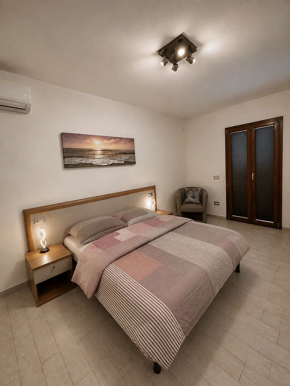 La Dolce Vita master bedroom in late afternoon with warm ambient lighting, coastal sunset canvas above the bed and air conditioning unit