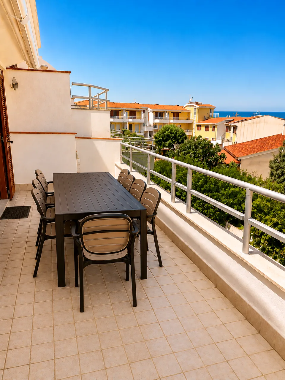 Front terrace with a long black outdoor dining table and eight chairs, sea visible beyond the rooftops