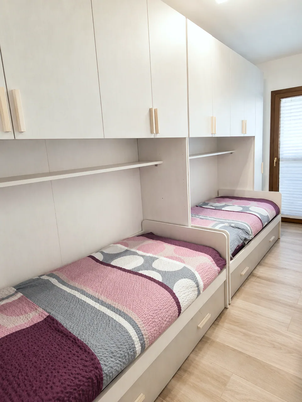 Twin bedroom at Il Paradiso showing both single beds with storage drawers, overhead cupboards and shelving beside the wooden balcony door