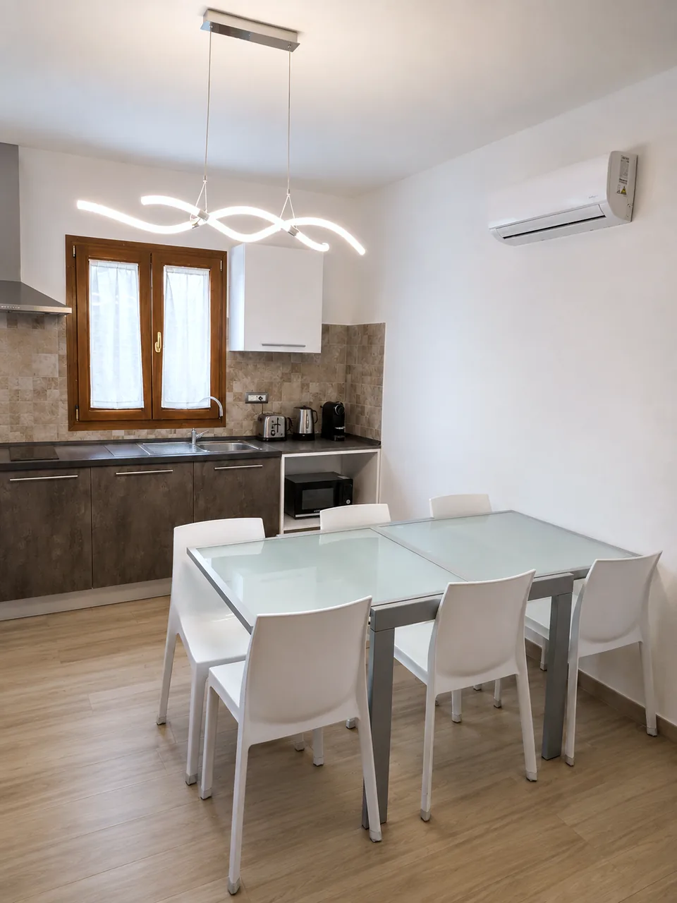 Bright dining area at Il Paradiso with an extendable glass table, six white chairs and the kitchen worktop with kettle, toaster, coffee machine and microwave