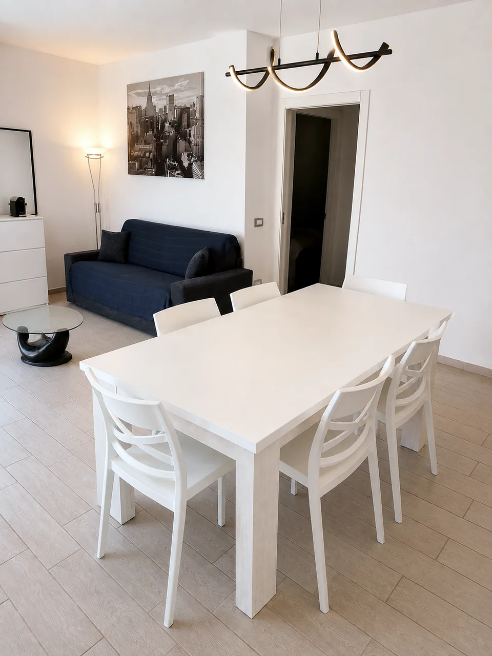 Dining table and lounge at La Dolce Vita in soft evening light, with the navy sofa and bedroom doorway beyond