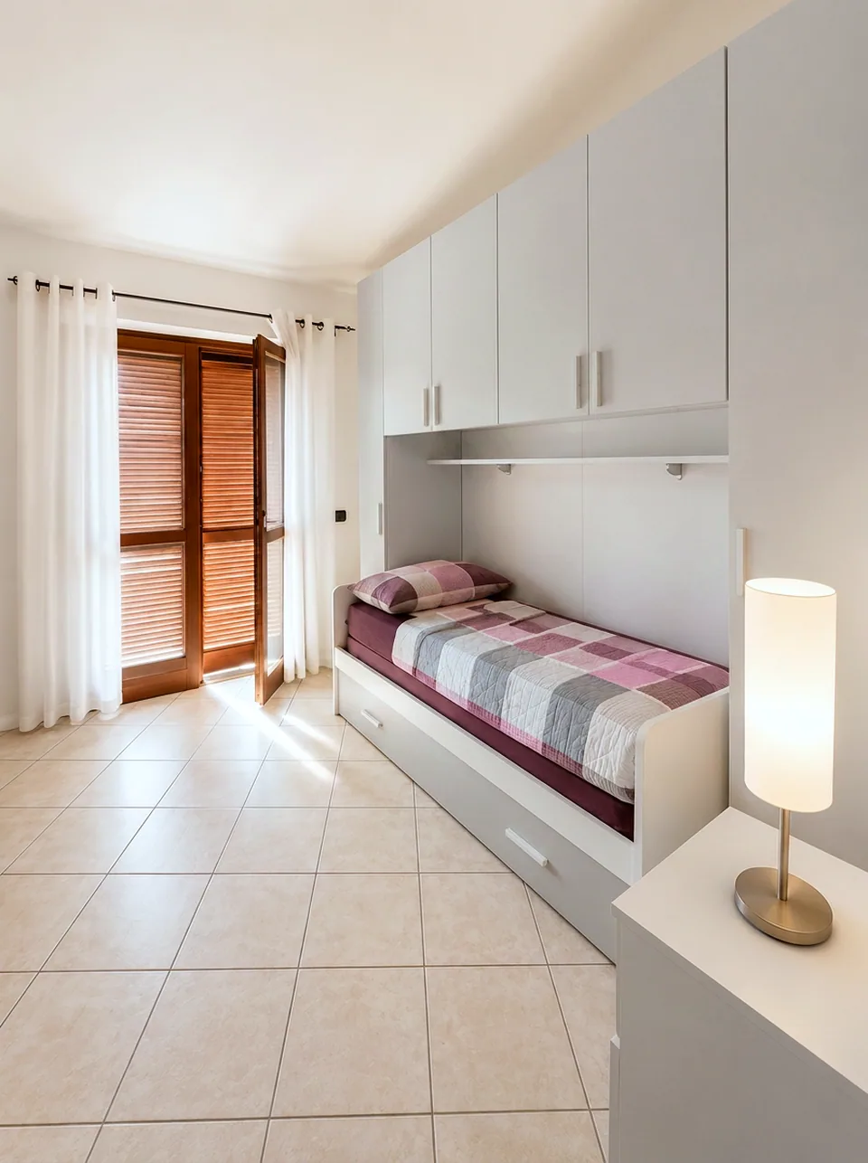 Second bedroom in the evening with warm lamplight and wooden shutters