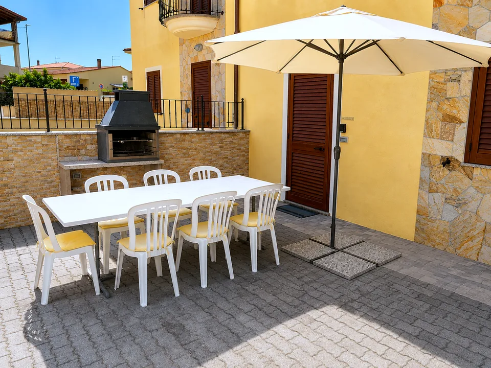 Private terrace at La Dolce Vita with a long white dining table, eight chairs, cream parasol and built-in stone barbecue