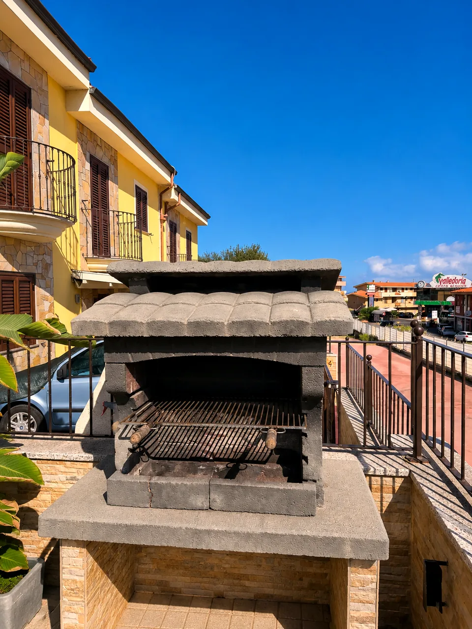 Built-in stone barbecue with grill on the private outdoor terrace under a clear blue Sardinian sky