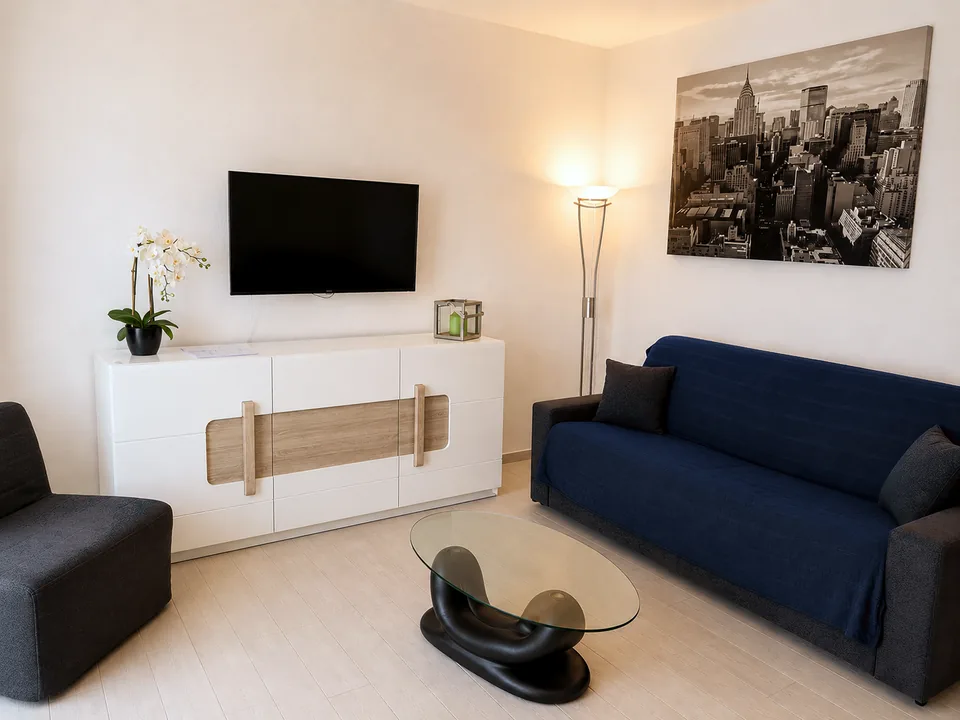 La Dolce Vita lounge in the evening, navy sofa and charcoal armchair lit by a warm floor lamp
