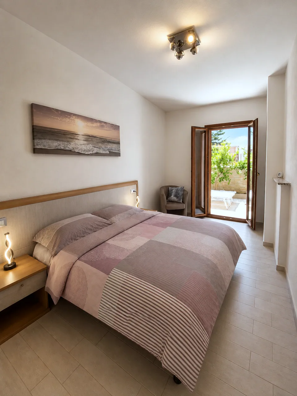 Master bedroom at La Dolce Vita in daylight, double bed with pink and grey bedding, oak bedside tables and open door to the private patio