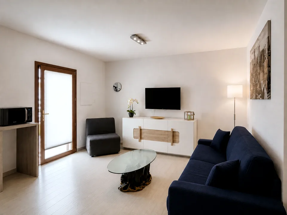 Living room at La Dolce Vita with navy sofa bed, wall-mounted smart TV, white sideboard and glass coffee table