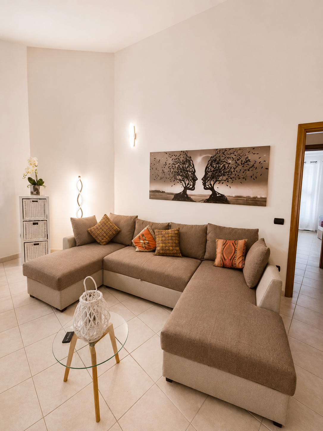 Lounge corner with large L-shaped sofa, glass side table and warm wall lighting